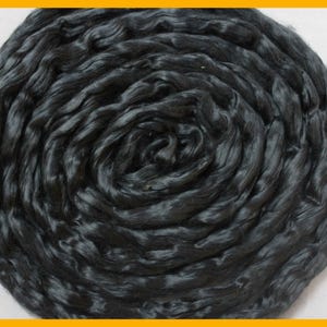 May include: A close-up shot of a tightly coiled bundle of black silk fibers. The fibers have a slightly glossy sheen, and the arrangement creates a swirling pattern. The texture appears soft and luxurious, suggesting a high-quality textile material.