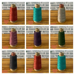 Peut inclure: Une collection de neuf bobines de fil individuelles disposées en grille, présentant diverses couleurs unies dont le rouge, le bleu sarcelle, l'argent, le mauve, le violet, le vert foncé et le noir, enroulées sur un noyau en carton.