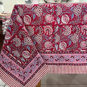 May include: A red and pink floral tablecloth with a white border. The tablecloth has a pink and white striped border with a floral pattern.