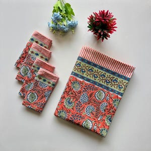 Puede incluir: Un juego de cuatro servilletas de color coral con estampado floral y un mantel a juego de color coral con borde a rayas blanco y verde y estampado floral.
