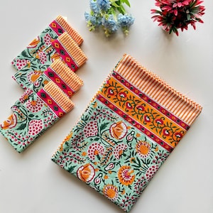 以下が含まれることがあります： ピンクとオレンジの縁取りが施された、緑とオレンジの花柄のナプキン6枚セット。ナプキンは折り畳まれ、白い表面に並べてあります。