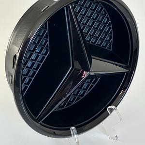 Emblema de estrela na grade dianteira Mercedes-Benz em preto brilhante ou prateado para os modelos W205, W117 e W118. Número da peça: A0008880060.