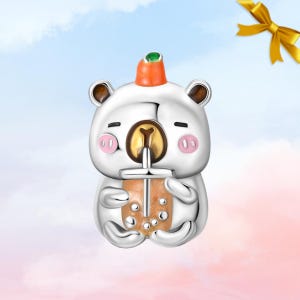 Könnte beinhalten: Ein silberner Charm in Form eines Bären, der einen Bubble Tea hält. Der Bär hat rosa Wangen, braune Ohren und einen kleinen orangefarbenen Hut mit einem grünen Edelstein. Der Bubble Tea ist hellbraun mit dunkelbraunen Blasen.