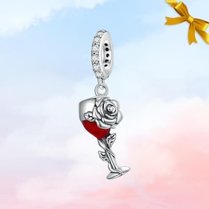 Puede incluir: Un charm de plata con una copa de vino llena de líquido rojo, con una rosa encima. El charm tiene un lazo incrustado con piedras transparentes. El tallo de la copa es una vid con hojas. El charm cuelga de un lazo plateado.