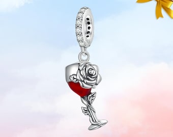 Könnte beinhalten: Ein silberner Charm-Anhänger mit einem Weinglas, das mit roter Flüssigkeit gefüllt ist und eine Rose aufweist. Der Charm hat eine mit klaren Steinen besetzte Schlaufe. Der Stiel des Glases ist eine Weinrebe mit Blättern. Der Charm hängt an einer Silberschlaufe.