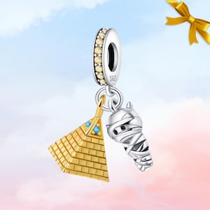 May include: A silver charm featuring a gold pyramid and a mummy pendant. The pyramid has blue accents, and the mummy is wrapped in bandages. The charm has a silver ring with yellow stones and the text "S925".