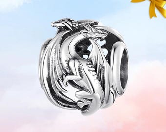 May include: A spherical silver charm bead featuring a detailed, three-dimensional dragon design with intricate scales, wings, and a coiled tail. The metal surface has a polished finish with darkened recessed areas to highlight the dragon's features.