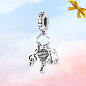 May include: A silver charm with a musical theme. The charm features a treble clef, a musical note, and a microphone with the word "Singer" engraved on it. The charm is connected to a round bead with a patterned design.