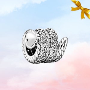 Peut inclure: Un charm en forme de serpent argenté, avec un corps enroulé et une tête relevée. Le corps du serpent est orné de petites pierres claires scintillantes. Le charm a un motif texturé détaillé sur son corps et sa tête, et un petit œil noir.