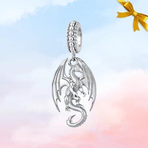 Könnte beinhalten: Ein silberfarbener Metallanhänger in Form eines detaillierten Drachen mit ausgebreiteten Flügeln und geringeltem Schwanz. Der Anhänger hängt an einer zylindrischen Perle mit texturierter, perlenartiger Oberfläche für Armbänder.