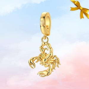 Könnte beinhalten: Ein goldfarbener Charm-Anhänger mit einem detaillierten Skorpion-Design. Der Anhänger hat oben eine Schlaufe zur Befestigung und hängt an einem goldfarbenen Verschluss. Der Skorpion hat detaillierte Klauen und einen gebogenen Schwanz.