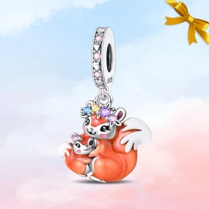 Könnte beinhalten: Ein silberner Charm mit zwei orangefarbenen Eichhörnchen mit weißen Akzenten, einem größeren und einem kleineren, die einen Blumenkranz aus blauen, gelben und violetten Steinen tragen. Die Öse ist mit rosa Steinen und Herzformen verziert, mit S925-Stempel.