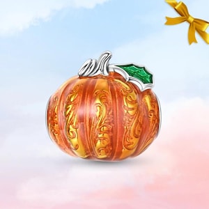 May include: A silver-toned pumpkin charm featuring a vibrant orange enamel finish with intricate gold-coloured filigree detailing. The pumpkin is topped with a metallic stem and a single green enamel leaf, creating a detailed seasonal accessory.