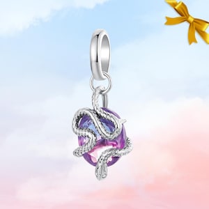 May include: A silver charm featuring a purple and pink oval gemstone, with a detailed silver snake wrapped around it. The charm has a loop at the top for attaching to a bracelet or necklace. The background is a gradient of blue, pink, and white.
