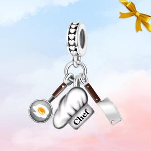 May include: Silver charm with a heart-patterned band, featuring a chef-themed design. Includes a frying pan with a fried egg, a chef's hat with the word "Chef", and a cleaver. The charm is suspended from a silver ring.