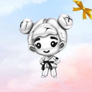Può includere: Un charm argentato raffigurante un personaggio dei cartoni animati in uniforme da karate con cintura nera. Il personaggio ha un viso sorridente, occhi neri e due chignon. Un nastro giallo sullo sfondo.