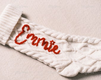Pode incluir: Meia de Natal branca de malha com o nome "Emme" bordado em vermelho.
