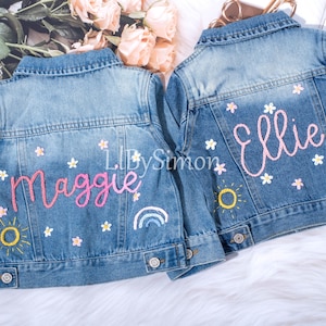 May include: Two denim jackets with embroidered names, Maggie and Ellie, and colorful floral designs. The jackets have a sun and rainbow design on the back.
