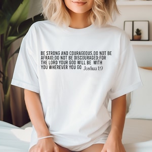 Puede incluir: Camiseta blanca con un gráfico de texto negro que dice "BE STRONG AND COURAGEOUS. DO NOT BE AFRAID;DO NOT BE DISCOURAGED;FOR THE LORD YOUR GOD WILL BE WITH YOU WHEREVER YOU GO Joshua 1:9"
