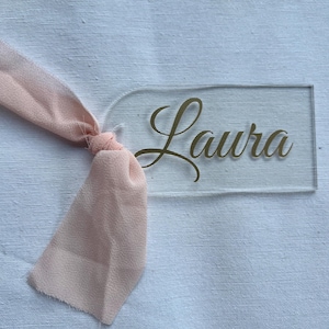 Marcasitios de Boda Personalizados | Metacrilato Transparente con Lazo de Gasa Rosa Claro y Nombre en Vinilo Dorado
