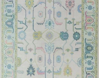 May include: A rectangular rug with a cream-colored background and a detailed floral pattern in pastel shades of blue, pink, green, and yellow. The rug has a border with repeating geometric and floral motifs, creating a symmetrical design.