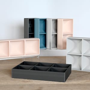 Könnte beinhalten: Eine Auswahl an geometrischen Aufbewahrungsbehältern in verschiedenen Farben, darunter Grau, Blau und Rosa. Die Behälter sind auf einer Holzoberfläche und einem transparenten Acrylständer angeordnet. Das Design weist mehrere Fächer auf.
