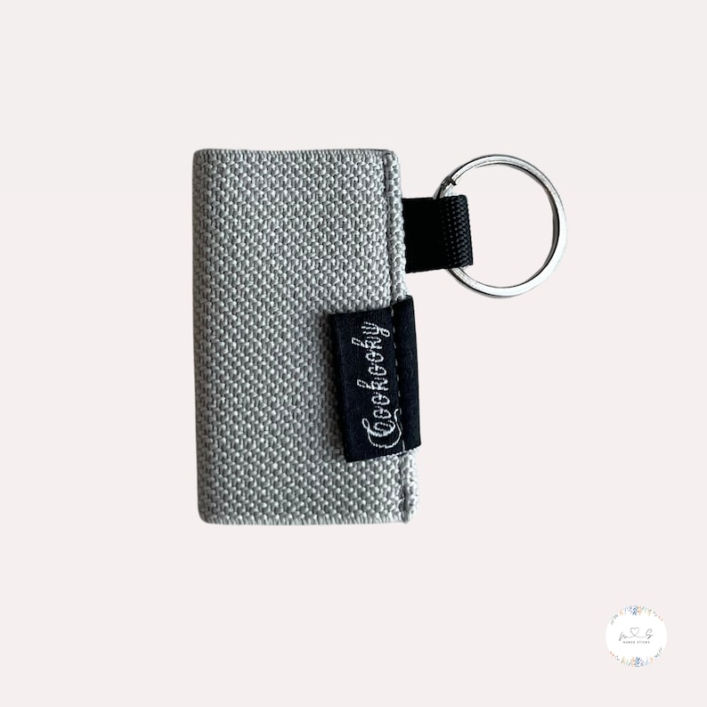 Peut inclure: Un porte-cl&eacute;s en tissu gris avec une &eacute;tiquette en tissu noir qui dit "Coolcocky".