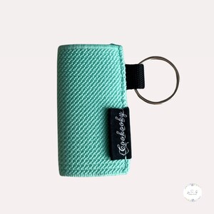 Peut inclure: Un porte-cl&eacute;s en tissu vert menthe avec une &eacute;tiquette noire qui dit "Cookeboogy". Le porte-cl&eacute;s a un anneau en m&eacute;tal argent&eacute;.