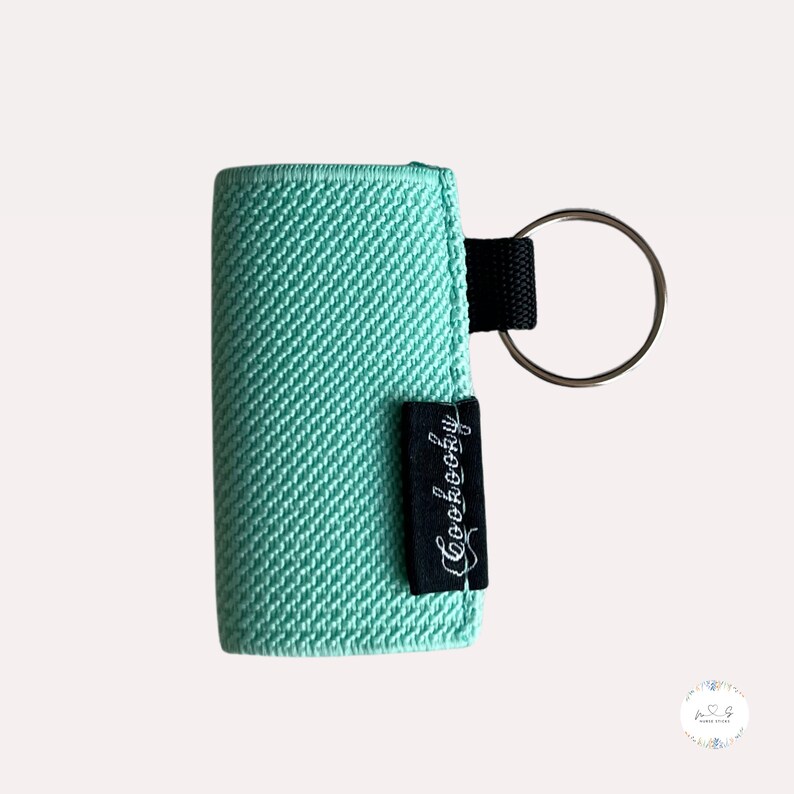 Peut inclure: Un porte-cl&eacute;s en tissu vert menthe avec une &eacute;tiquette noire qui dit "Cookeboogy". Le porte-cl&eacute;s a un anneau en m&eacute;tal argent&eacute;.