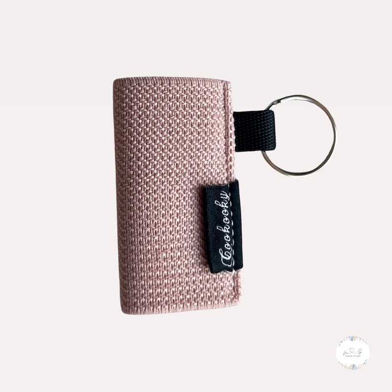 Peut inclure: Un porte-cl&eacute;s en tissu rose avec une sangle noire et un anneau argent&eacute;. Le porte-cl&eacute;s porte l'inscription "Cuckoooky".