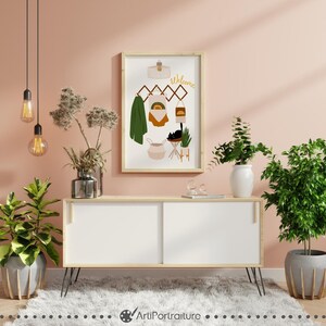 May include: A framed illustration of a welcome sign with a rainbow, a cat, a basket, and a plant. The illustration is hanging on a wall with a light pink background.