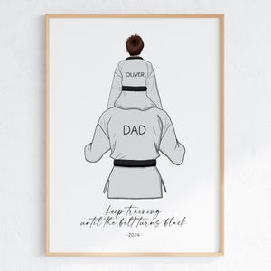 Könnte beinhalten: Eine Schwarzweißillustration eines Vaters und seines Sohnes in Kampfkunstuniformen. Der Vater steht mit seinem Sohn auf den Schultern. Die Uniform des Sohnes trägt den Schriftzug "OLIVER" und die des Vaters "DAD". Der Text darunter lautet "Trainiere weiter, bis der Gürtel schwarz wird - 2024 -"