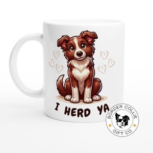 Puede incluir: Taza de cerámica blanca con un perro border collie de dibujos animados marrón y blanco. El perro está sentado y mirando al espectador. La taza tiene el texto "I herd ya" y un logotipo para "Border Collie Gift Co."