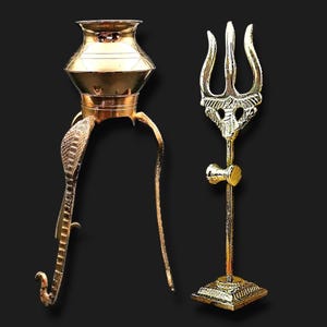 Può includere: Due manufatti religiosi color oro su sfondo nero. Uno è un vaso a forma di pentola con un supporto a forma di cobra. L'altro è un tridente con un elemento a forma di martello alla base. Entrambi gli oggetti hanno dettagli intricati e una finitura lucida.
