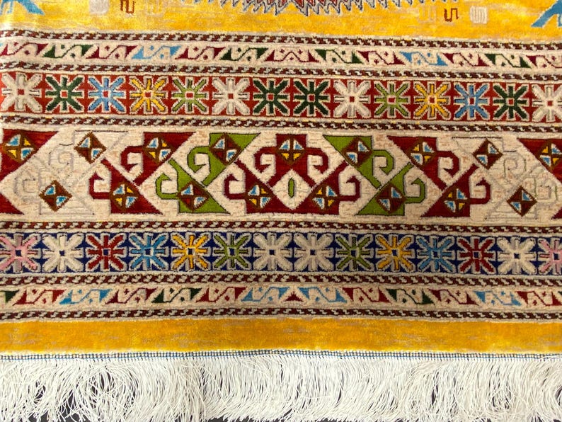 K&ouml;nnte beinhalten: Nahaufnahme eines gelb-cremefarbenen Teppichs mit komplizierten geometrischen Mustern. Der Teppich weist ein sich wiederholendes Design aus floralen und geometrischen Formen in Rot, Gr&uuml;n, Blau und Gelb auf. Der Teppich hat einen Fransenrand.