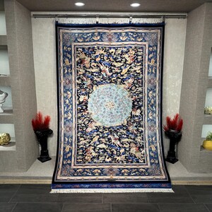 Peut inclure: Un grand tapis persan orné, avec un fond bleu marine et un médaillon central. Le tapis présente des motifs complexes, des figures et une bordure détaillée. Il est exposé sur un mur, mettant en valeur sa taille et son design.