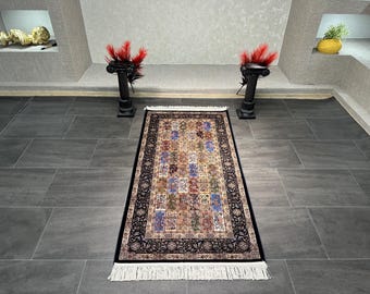 Puede incluir: Alfombra rectangular con un diseño detallado y colorido. La alfombra presenta un diseño central de varios cuadrados en tonos azules, rojos, verdes y beige, enmarcado por un borde negro con motivos florales. Flecos blancos en los extremos.