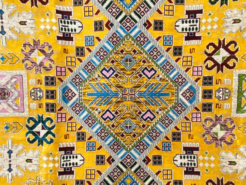 K&ouml;nnte beinhalten: Nahaufnahme eines gelben Teppichs mit einem komplizierten geometrischen Muster. Das Design zeigt Rauten, Quadrate und stilisierte Blumenmotive in Blau-, Rosa-, Braun- und Gr&uuml;nt&ouml;nen. Der Teppich hat ein detailliertes, strukturiertes Aussehen.