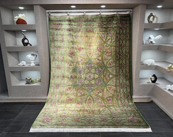 Könnte beinhalten: Ein großer, rechteckiger grüner Teppich mit einem komplizierten Blumenmuster. Der Teppich hat ein zentrales Medaillon-Design mit roten, blauen und goldenen Akzenten. Der Teppich hat einen Fransenrand und wird in einem Raum mit Einbauregalen ausgestellt.