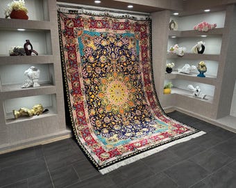 Könnte beinhalten: Ein großer, verzierter Teppich mit einem zentralen Medaillon-Design. Der Teppich hat einen marineblauen Hintergrund mit floralen Mustern in Gelb, Rot und Blau. Der Rand ist rot mit aufwendigen Details, und der Teppich hat einen weißen Fransen.