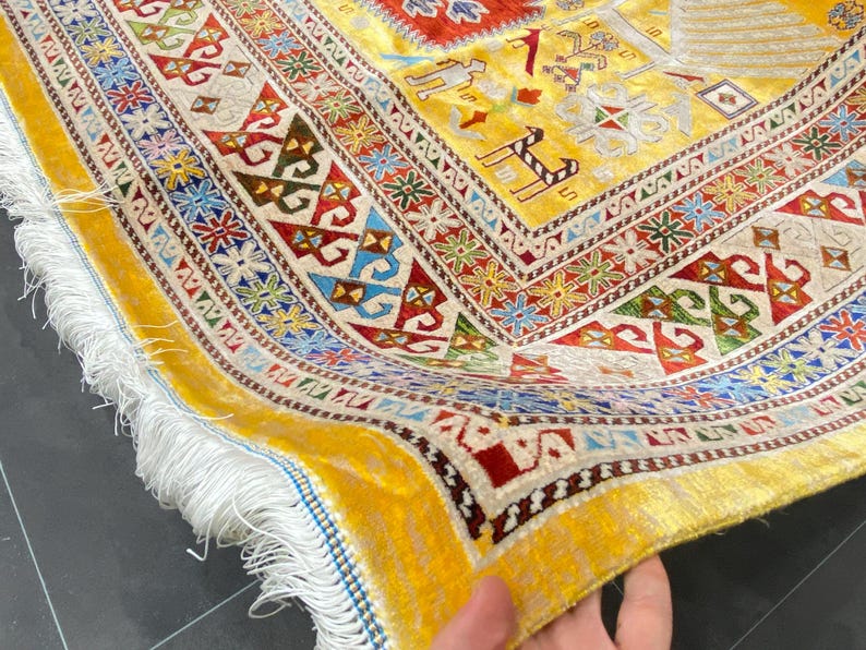 K&ouml;nnte beinhalten: Nahaufnahme eines lebendigen, handgewebten Teppichs mit gelbem Hintergrund und komplizierten geometrischen Mustern in Rot, Blau, Gr&uuml;n und Wei&szlig;. Der Teppich hat einen Fransenrand und einen detaillierten Rand.