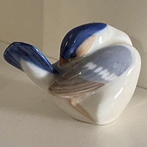 May include: A porcelain figurine of a bluebird with a white and blue body and brown wings. The bird is curled up in a sleeping position.