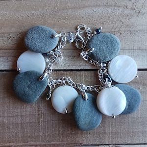 May include: A silver chain bracelet with multiple charms. The charms are made of smooth, gray stones and white, pearlescent discs.