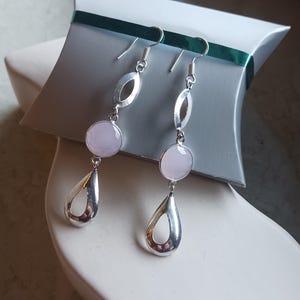 May include: A pair of silver dangle earrings with pink gemstone accents. The earrings feature a teardrop shape with a cutout design and a round gemstone.