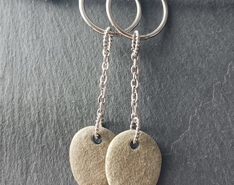 May include: A pair of silver hoop earrings with a chain and a smooth, gray stone pendant on each earring.