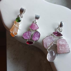 Könnte beinhalten: Drei silberne Anhänger mit verschiedenen Edelsteinen. Der erste Anhänger zeigt einen Cluster aus rosa und roten Edelsteinen. Der zweite Anhänger zeigt einen Cluster aus rosa und roten Edelsteinen. Der dritte Anhänger zeigt einen Cluster aus rosa und roten Edelsteinen.