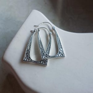 May include: A pair of silver hoop earrings with a floral design. The earrings are shaped like a rectangle with rounded corners.
