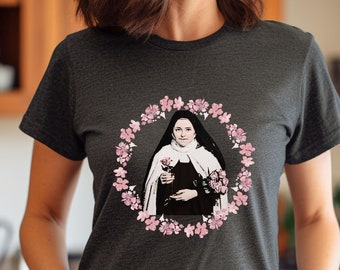 Puede incluir: Una camiseta gris oscuro con un estampado gráfico de una mujer con hábito de monja sosteniendo una rosa. El gráfico está rodeado por una corona de flores rosas.