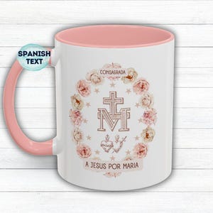 May include: White ceramic mug with a pink interior and handle. The mug features a floral wreath design with a cross and the text "CONSAGRADA" and "A JESUS POR MARIA".