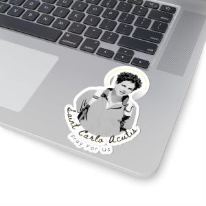 May include: A black and white sticker featuring a photo of a young man with a halo above his head. The text "Saint Carlo Acutis Pray For Us" is written in a cursive font around the photo.